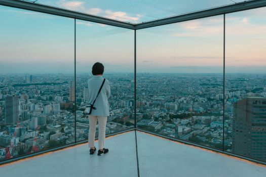 A person gazes over Tokyo's skyline from Shibuya Sky during sunset.