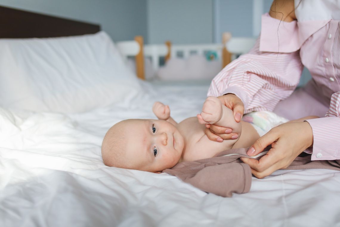 Mother gently dressing her newborn baby on a soft bed