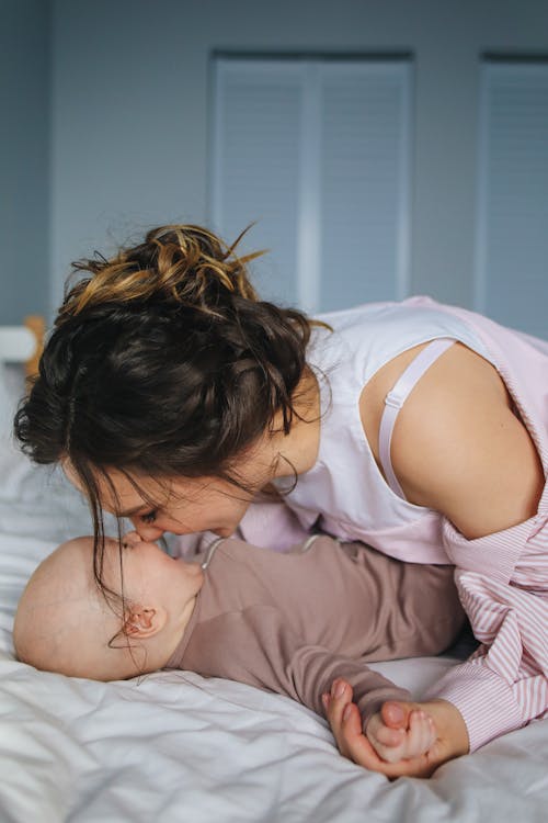 Mulher Em Camisa De Manga Comprida Listrada De Branco E Rosa Brincando Com O Bebê Deitado Na Cama