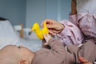 一位充满爱心的母亲和她的婴儿在舒适的卧室里玩着黄色玩具