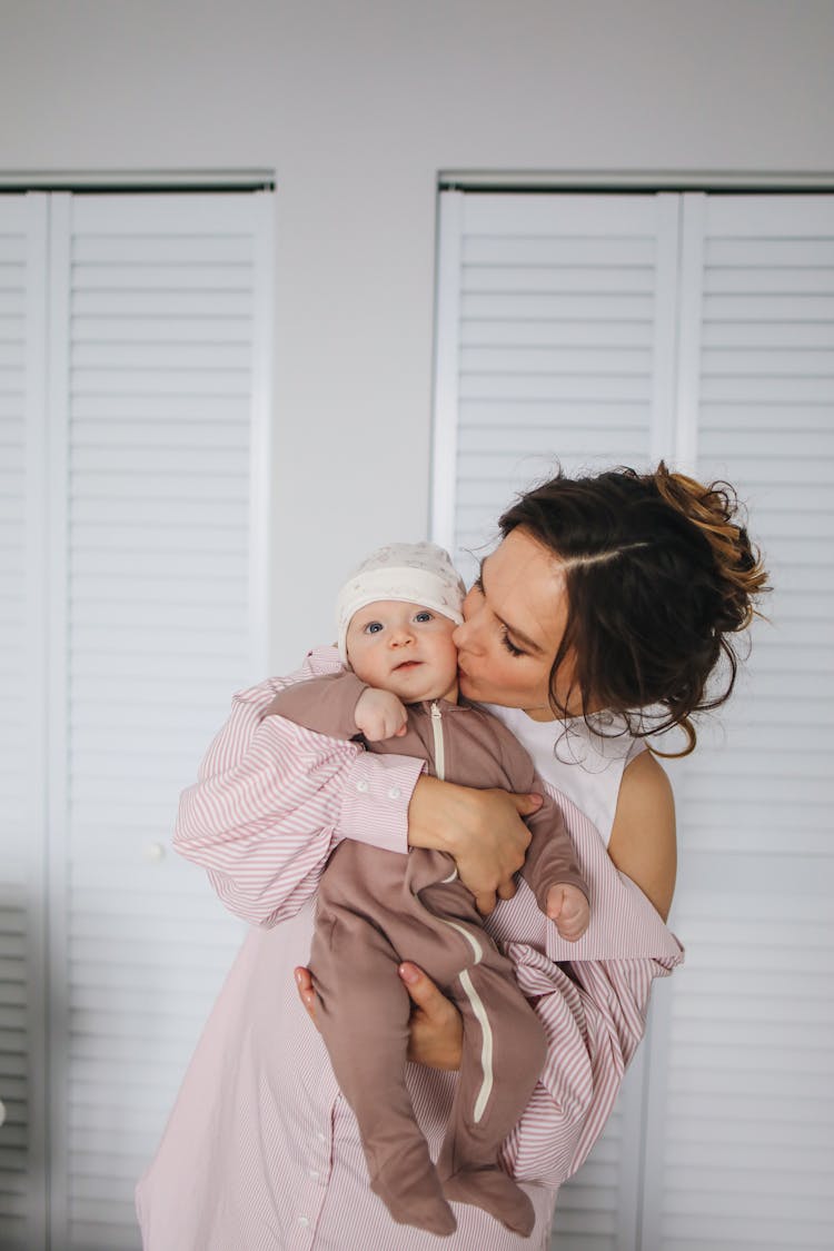 Woman In Pink And White Striped Dress Carrying Baby Wearing Brown Onesie