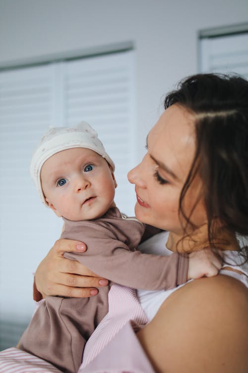 Free Woman in White and Pink Striped Top Carrying Baby Wearing Brown Onesie Stock Photo