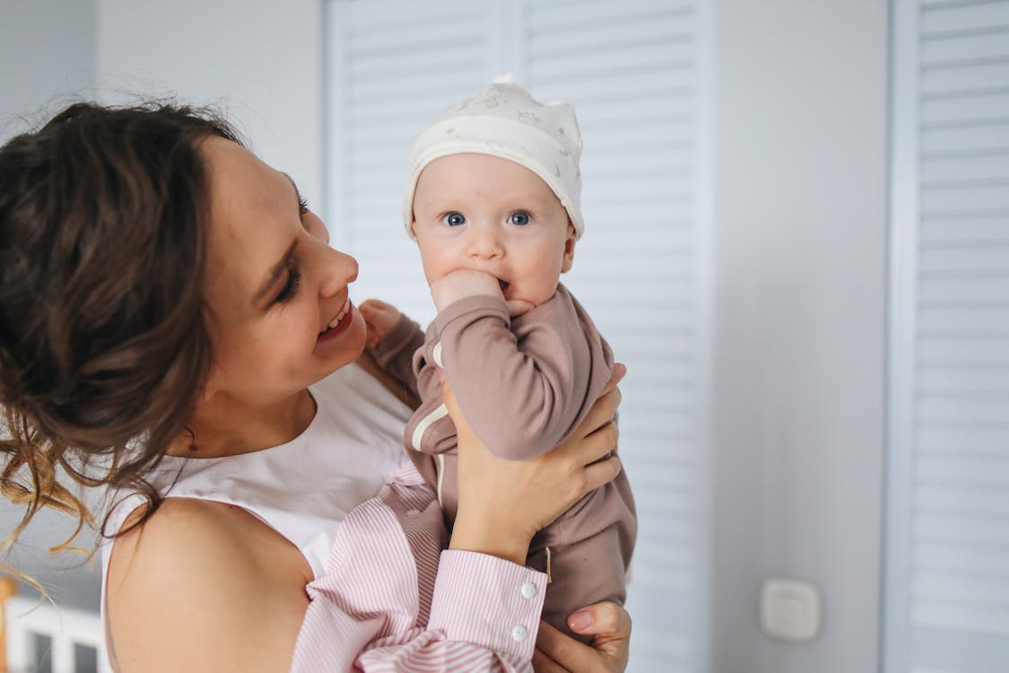 Free Woman in White and Pink Striped Long Sleeve Shirt Carrying Baby Wearing Brown Onesie Stock Photo