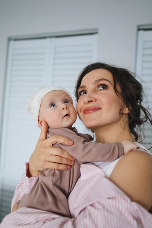 Free Woman in White and Pink Striped Long Sleeve Shirt Carrying Baby Wearing Brown Onesie Stock Photo