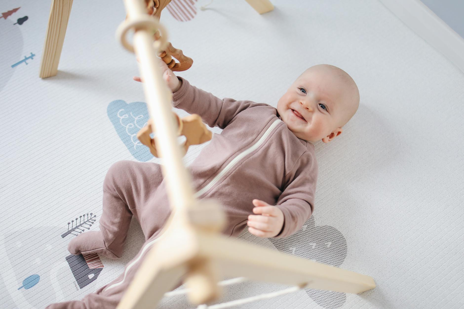 A joyful baby lying on a soft mat, playing with wooden toys, smiling brightly.