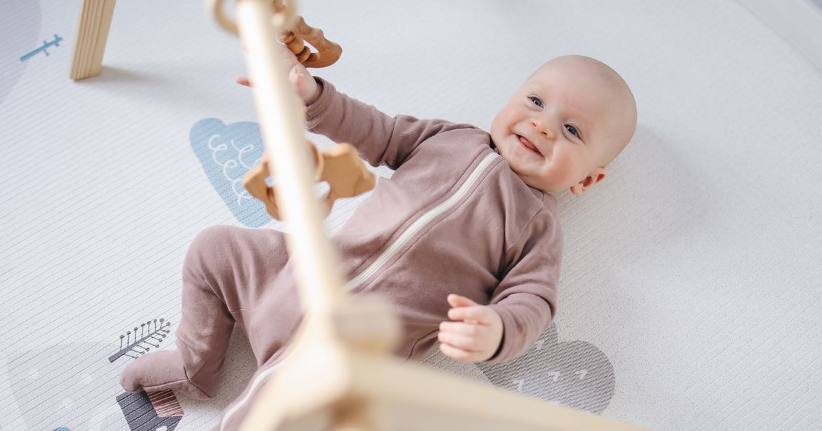 A smiling baby lying under a wooden baby play gym