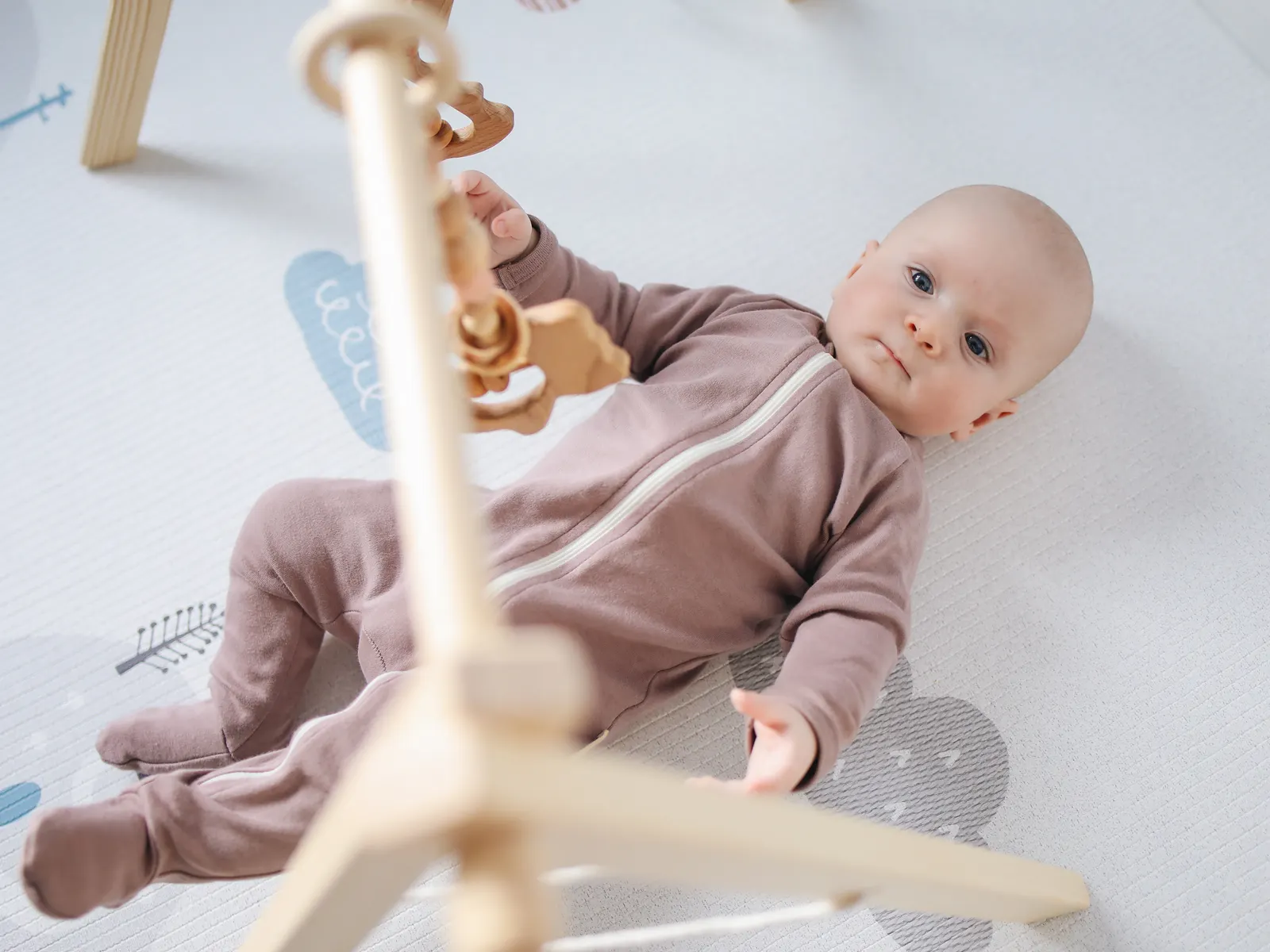 Baby in a cozy onesie playing with wooden toys on a soft mat