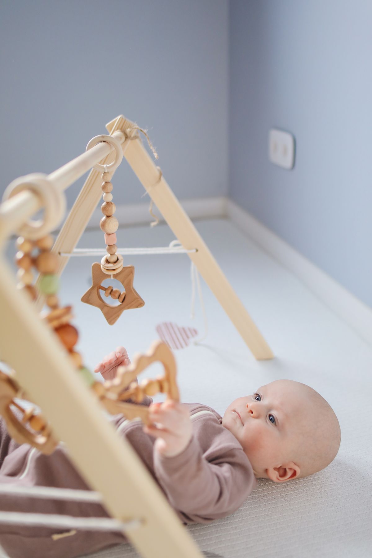 Baby lying on the floor playing with a wooden rattle toy in a bright room
