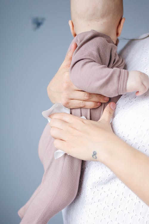 Person in White Top Carrying Baby Wearing Brown Onesie