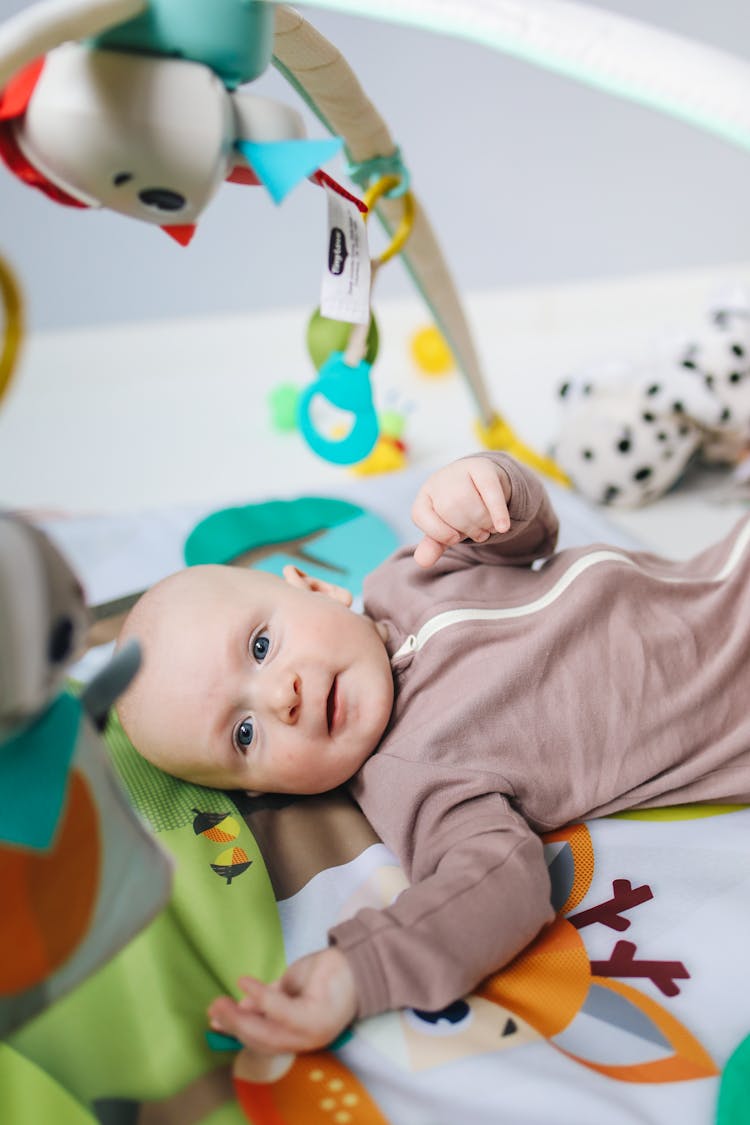 Baby In Brown Onesie Lying On Bed