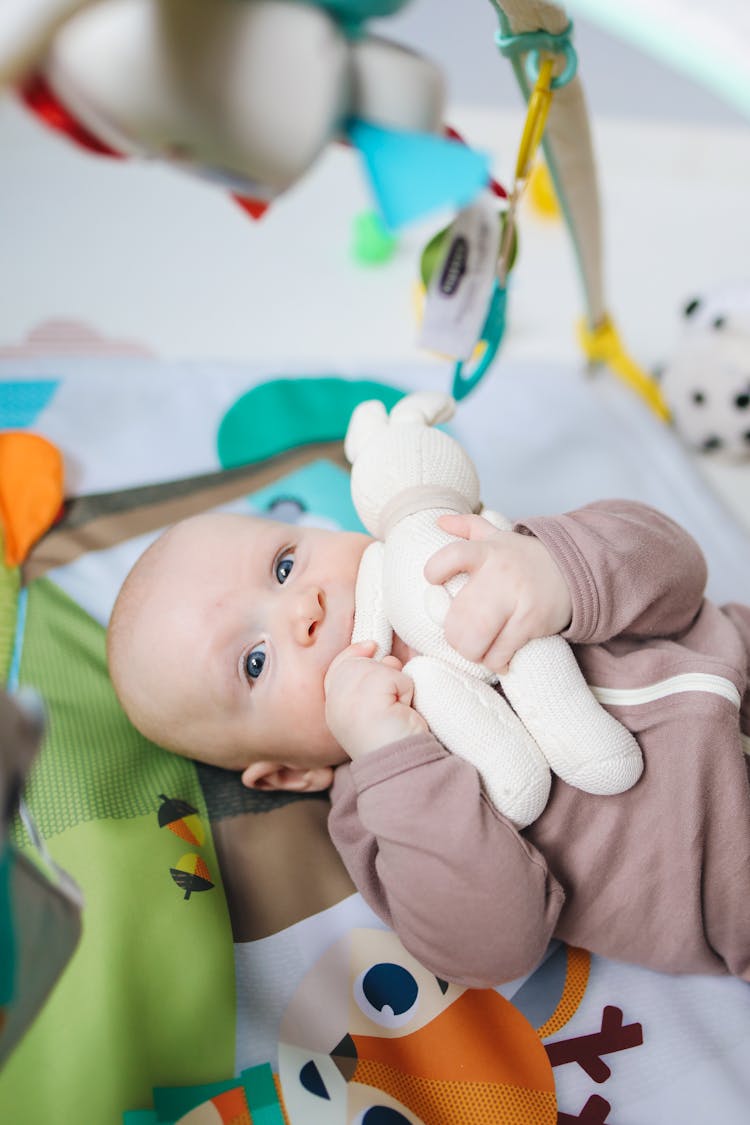 Baby In Onesie Lying On Green And Blue Mat