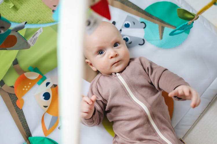 Baby In Pink Zip Up Onesie Lying On Themed Baby Mat