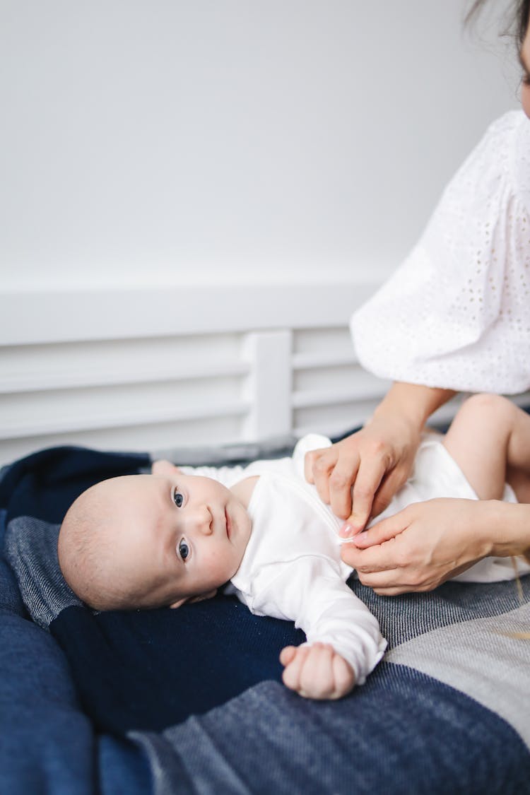 Baby In White Onesie Lying On Bed