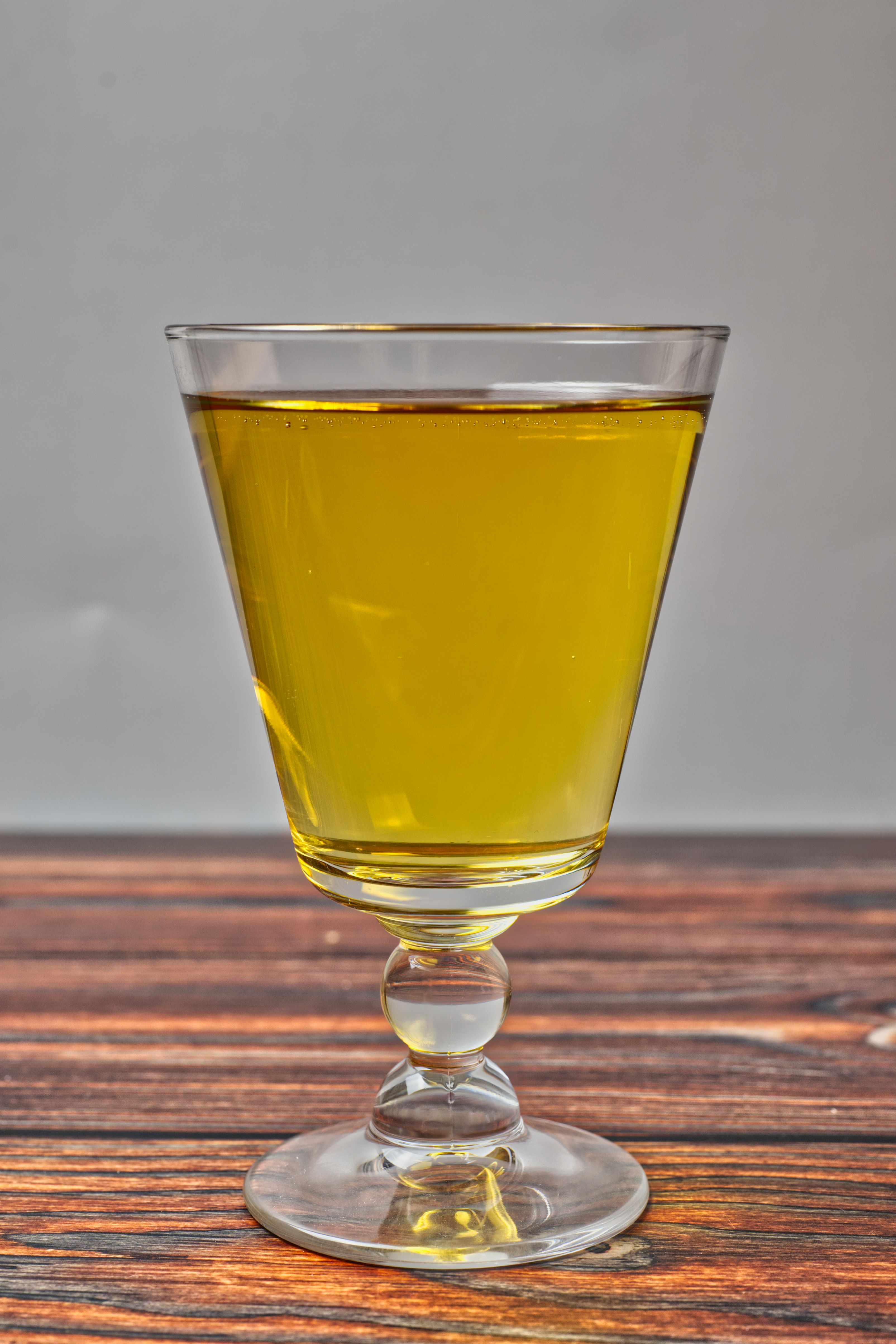 A clear glass of yellow juice elegantly displayed on a wooden surface with a neutral background.