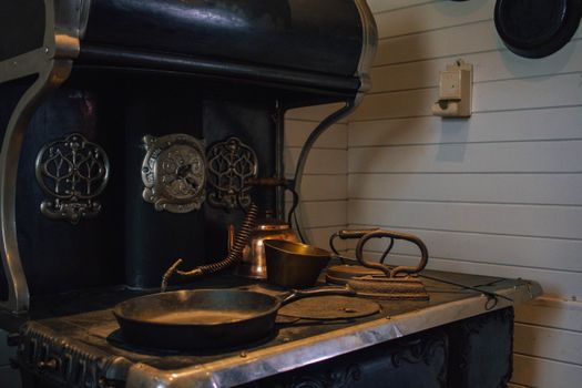 A close-up of a vintage cast iron stove with pots and utensils in a rustic kitchen setting.