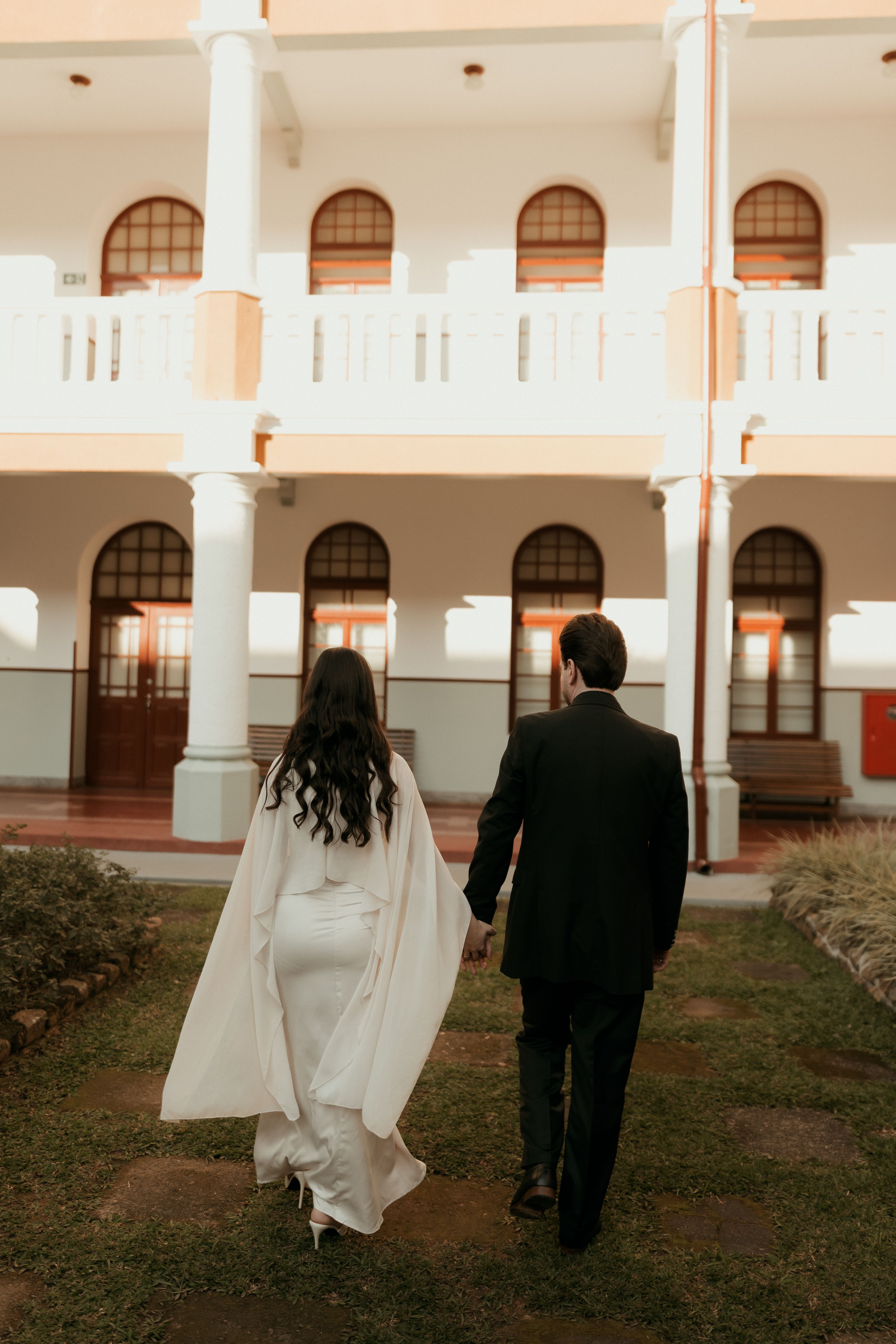An elegant couple walking through a classic courtyard, captured in warm light.