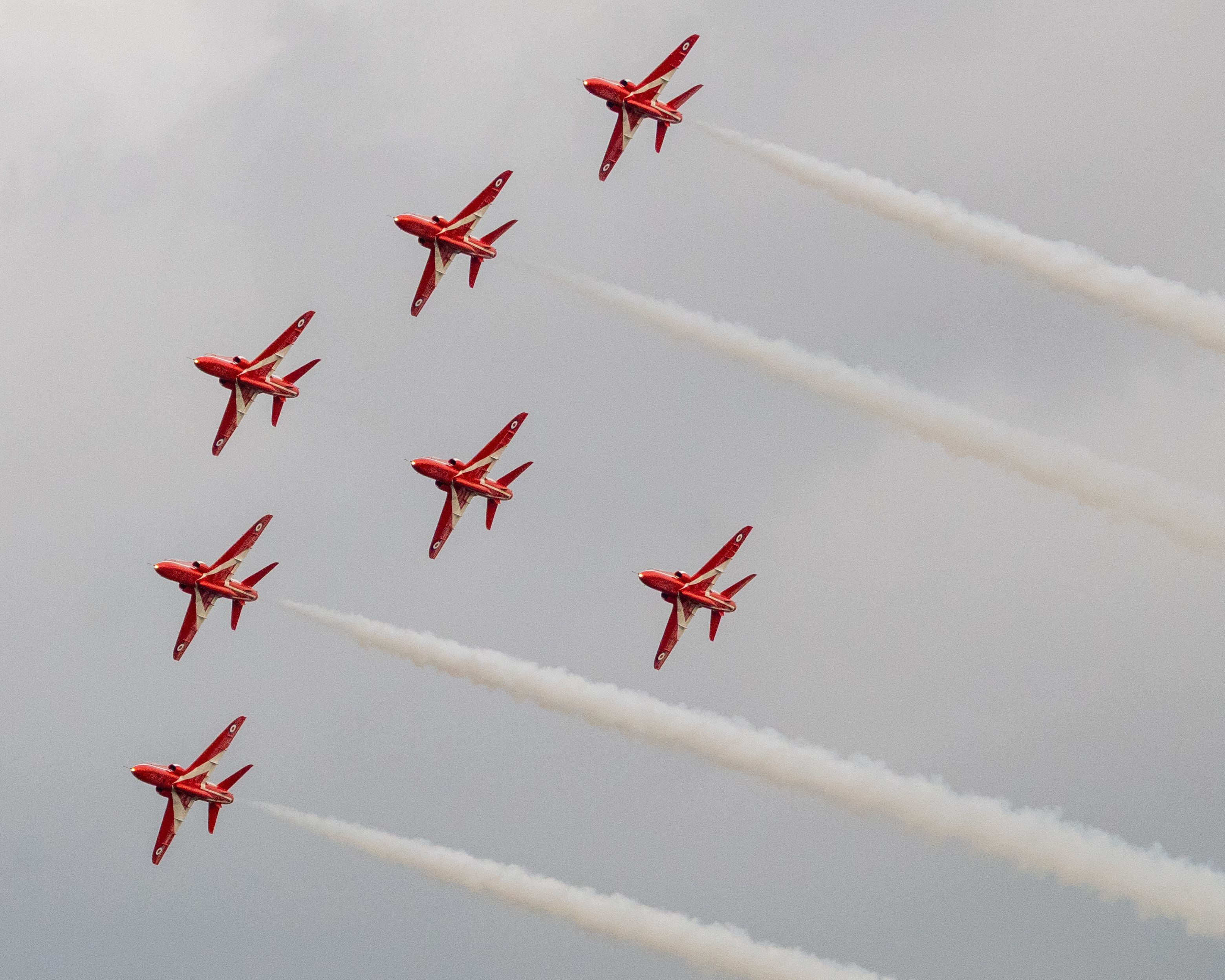Stunning formation of red jets flying in unison with smoke trails on a cloudy day.