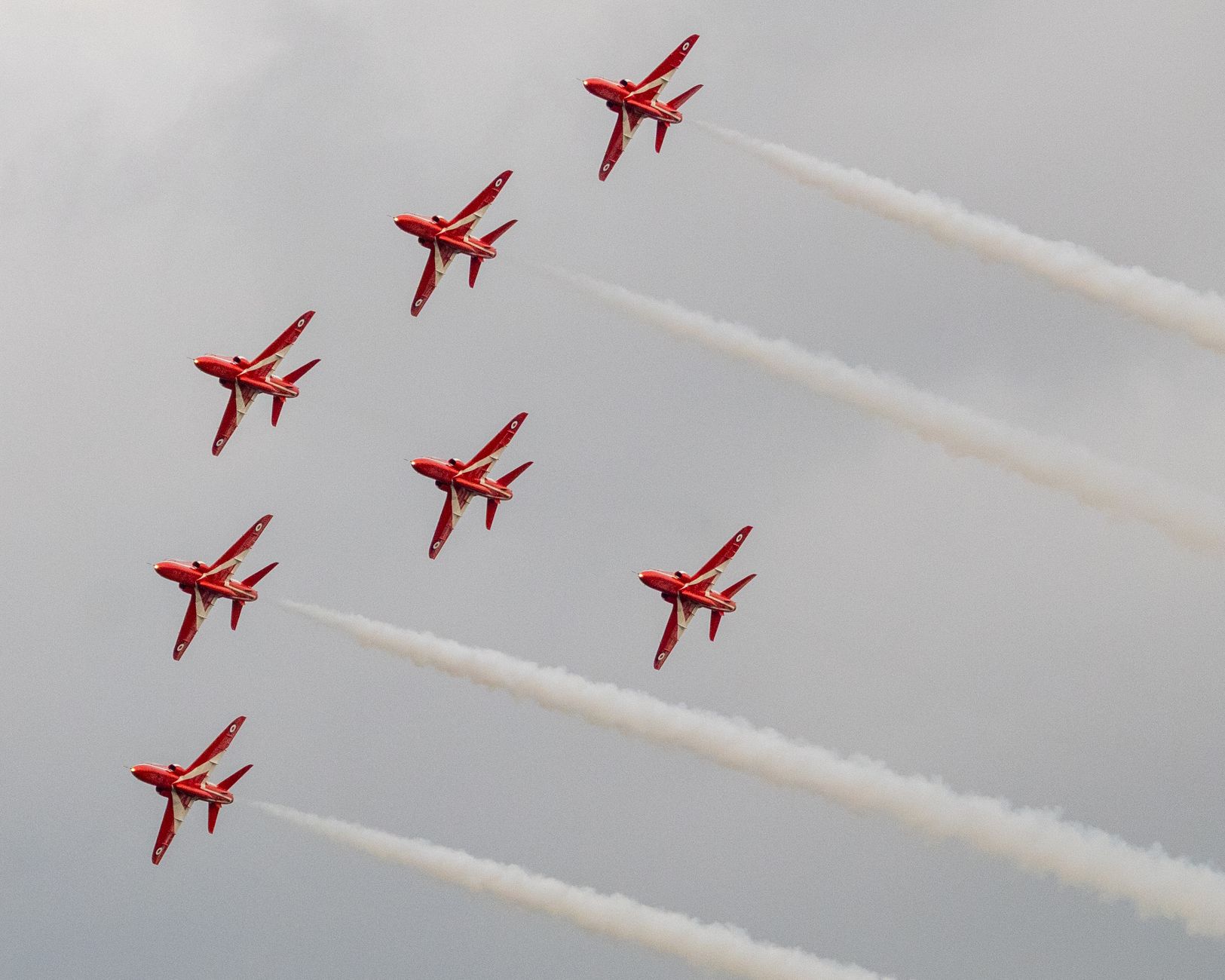 Stunning formation of red jets flying in unison with smoke trails on a cloudy day.
