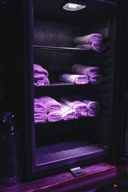 Opened door of sterilizer cabinet with ultraviolet light disinfecting fresh folded towel on shelves