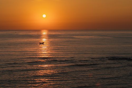Free A tranquil sunset over the ocean with a small fishing boat in Cua Tung, Vietnam. Stock Photo