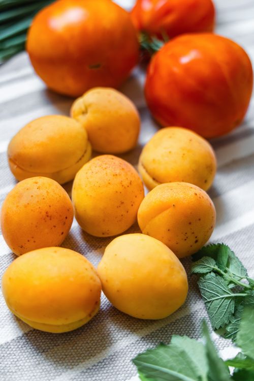 Free Bright apricots and tomatoes on a table with greens, perfect for summer-themed stock photos. Stock Photo