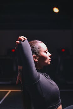 Side view of a young woman stretching her arms indoors with focused determination.