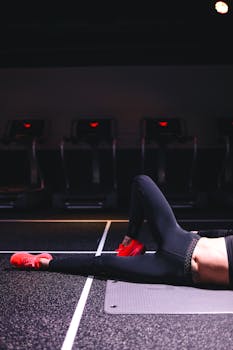 Unrecognizable female in sportswear and red sneakers lying on mat and doing exercises with bent leg in modern fitness center