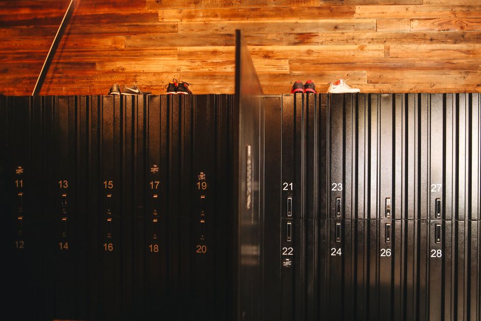 Stylish locker room in gym with wooden walls and steel black lockers with sneakers placed on roof of lockers divided by partition