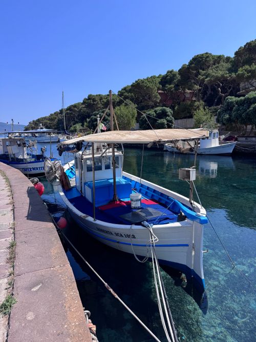 Free A vibrant fishing boat docked in a serene Sardinia harbor, surrounded by lush greenery and clear blue waters. Stock Photo