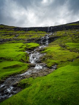 Beautiful waterfall flowing down mossy hills under a cloudy sky. Ideal for nature and travel content.