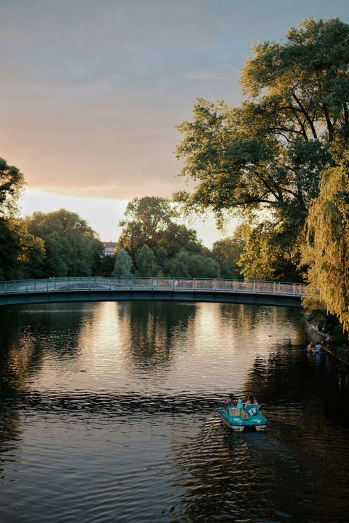 Free A tranquil view of Alster Lake in Hamburg with people relaxing on a paddle boat under a sunset sky. Stock Photo