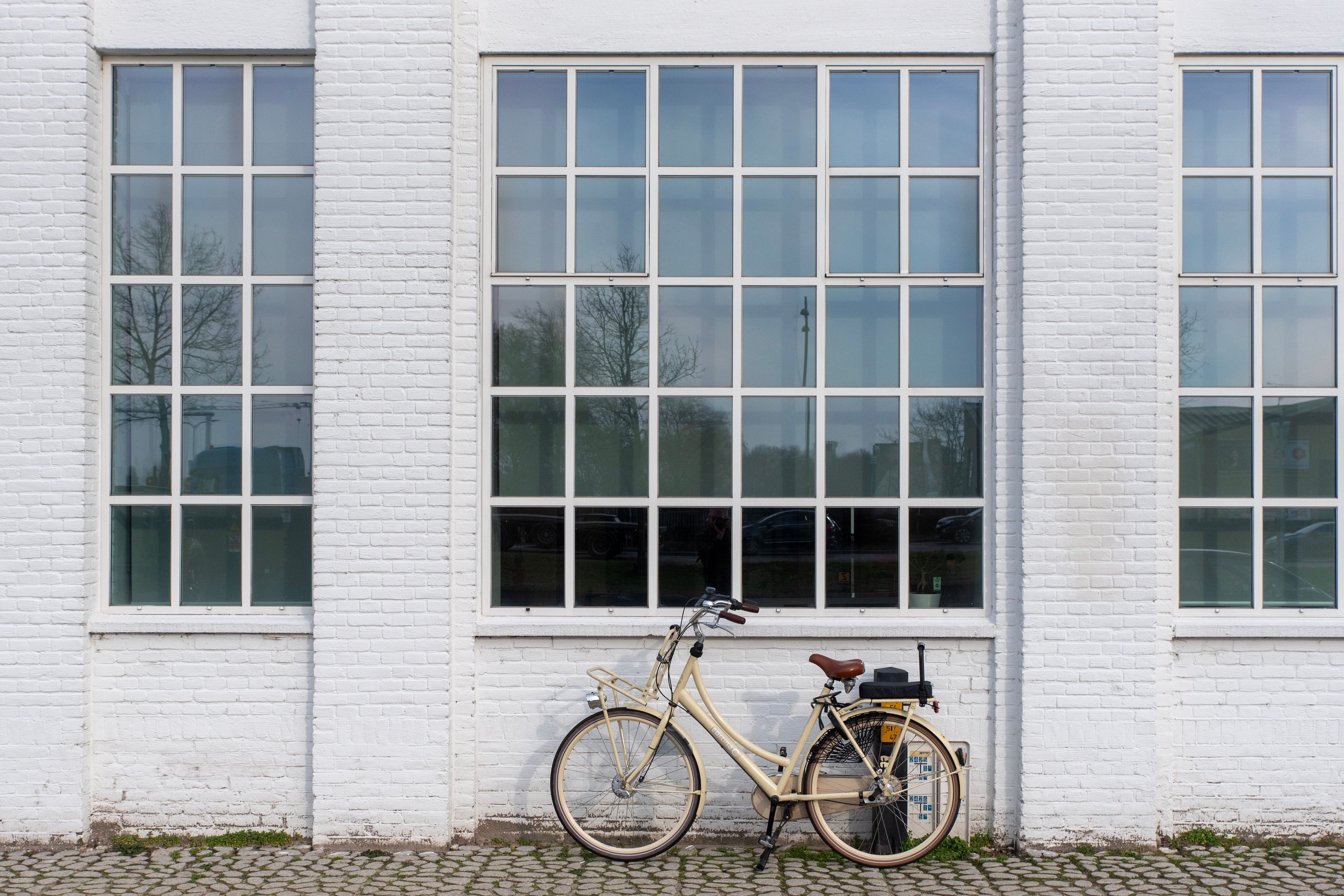 A vintage-style bicycle parked in front of a white brick building with large windows.