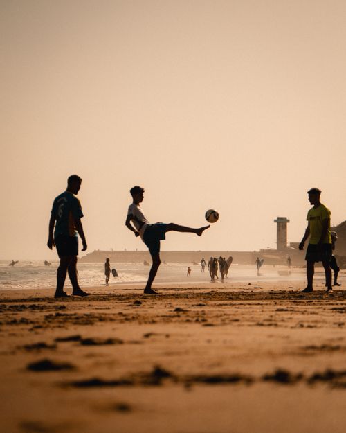 Free Silhouetted teens enjoy a soccer game on the beach during a stunning sunset. Stock Photo
