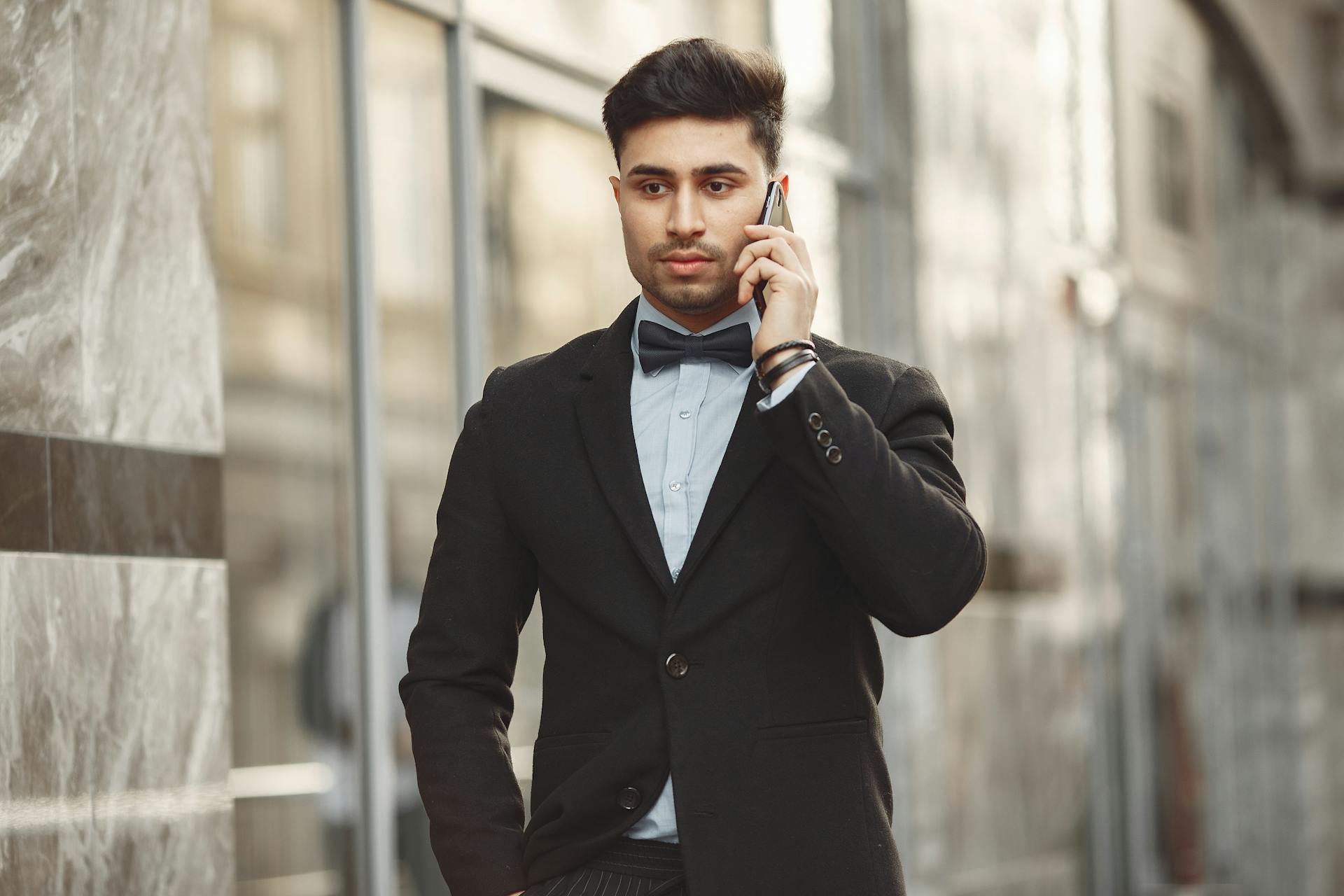 Portrait of a focused businessman using a smartphone, dressed in a suit with a bow tie, outdoors.