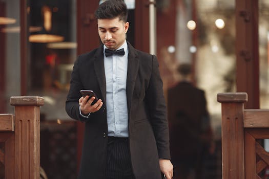 A man in a suit checks his phone while standing outdoors during the day.