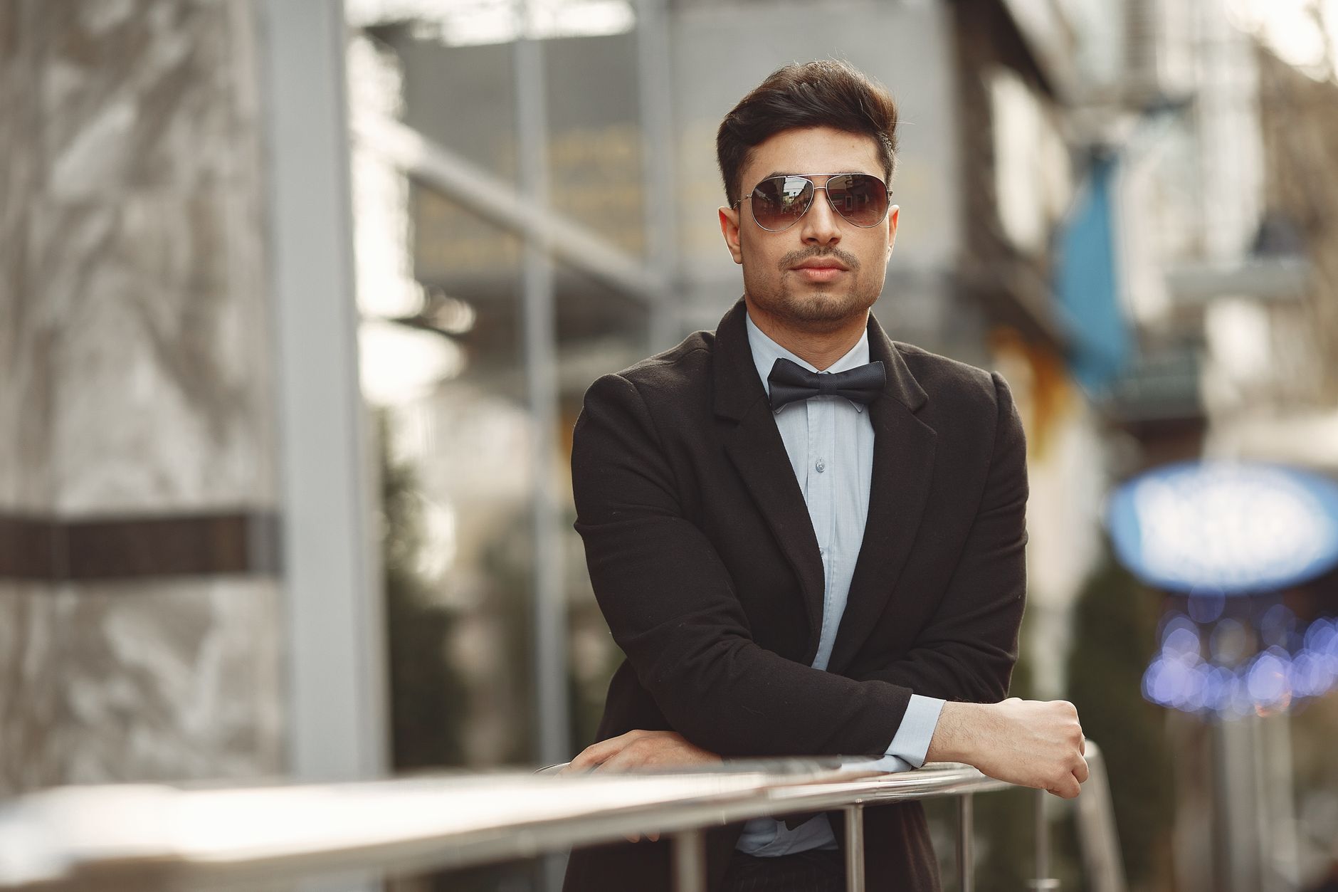 A stylish man in sunglasses and bow tie, exuding confidence in an urban setting.