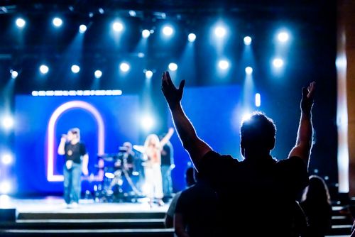 Free Silhouetted audience member raising hands during a live concert performance with vibrant stage lights. Stock Photo