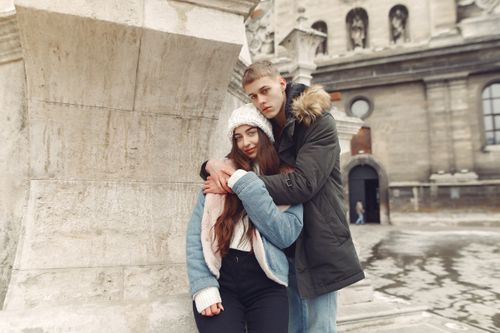 Free A couple warmly embracing outdoors in front of historic architecture during winter. Stock Photo