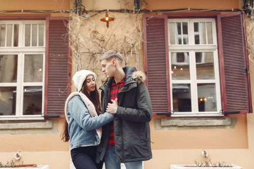 Free Young man and woman in warm clothes standing together on city street against old building and holding hands together during romantic date Stock Photo