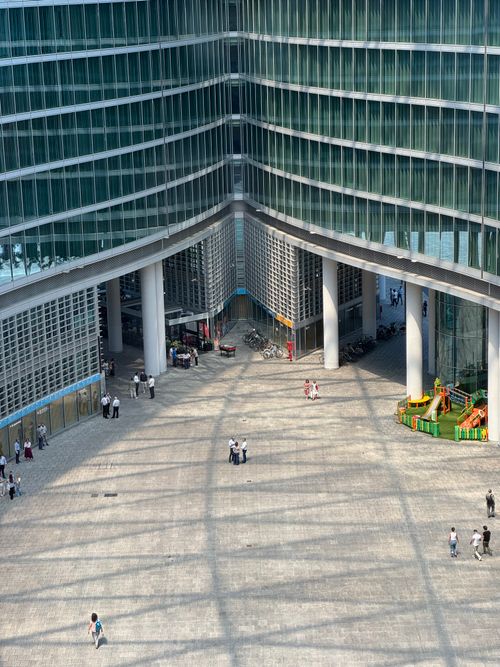 Free Aerial perspective of a modern skyscraper courtyard in Milan, featuring shadows and scattered people. Stock Photo