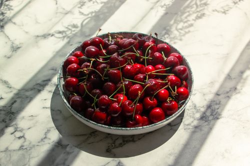 Free A bowl of ripe red cherries on a marble table in sunlight. Perfect for fruit and summer themes. Stock Photo