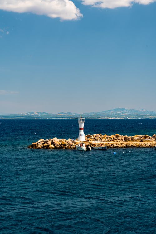 Free A scenic view of a lighthouse on a rocky outcrop by the sea under a clear blue sky. Stock Photo