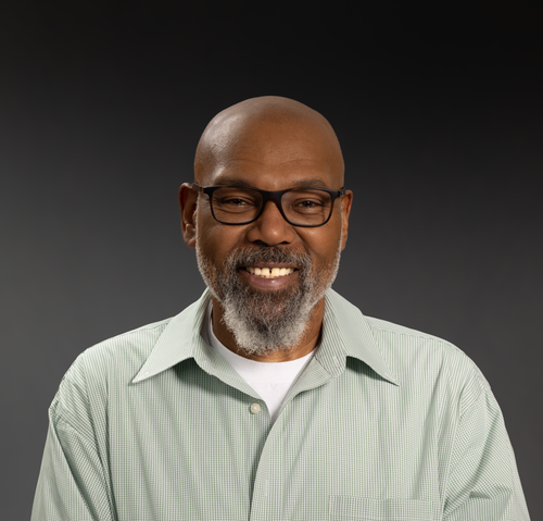 Free Portrait of a smiling elderly man with glasses, beard, in a green shirt on a dark background. Stock Photo