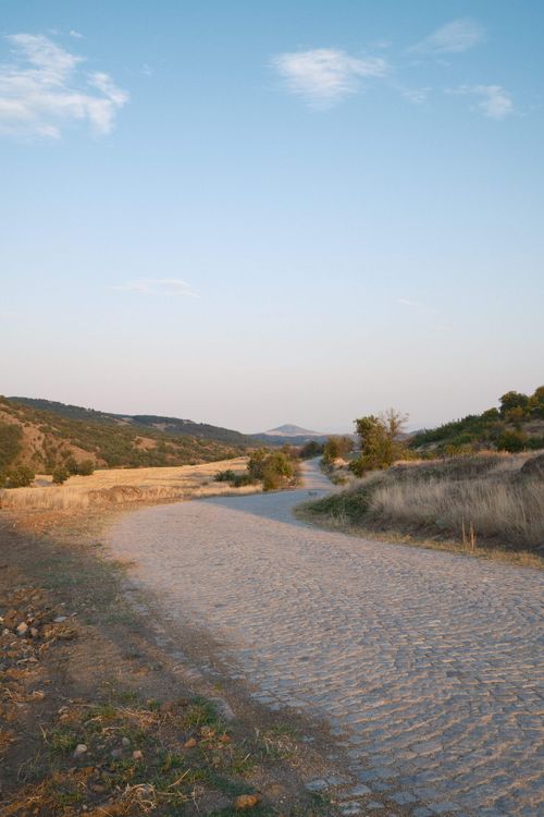 Free A tranquil rural road in Bulgaria during sunset with rolling hills and open fields. Stock Photo