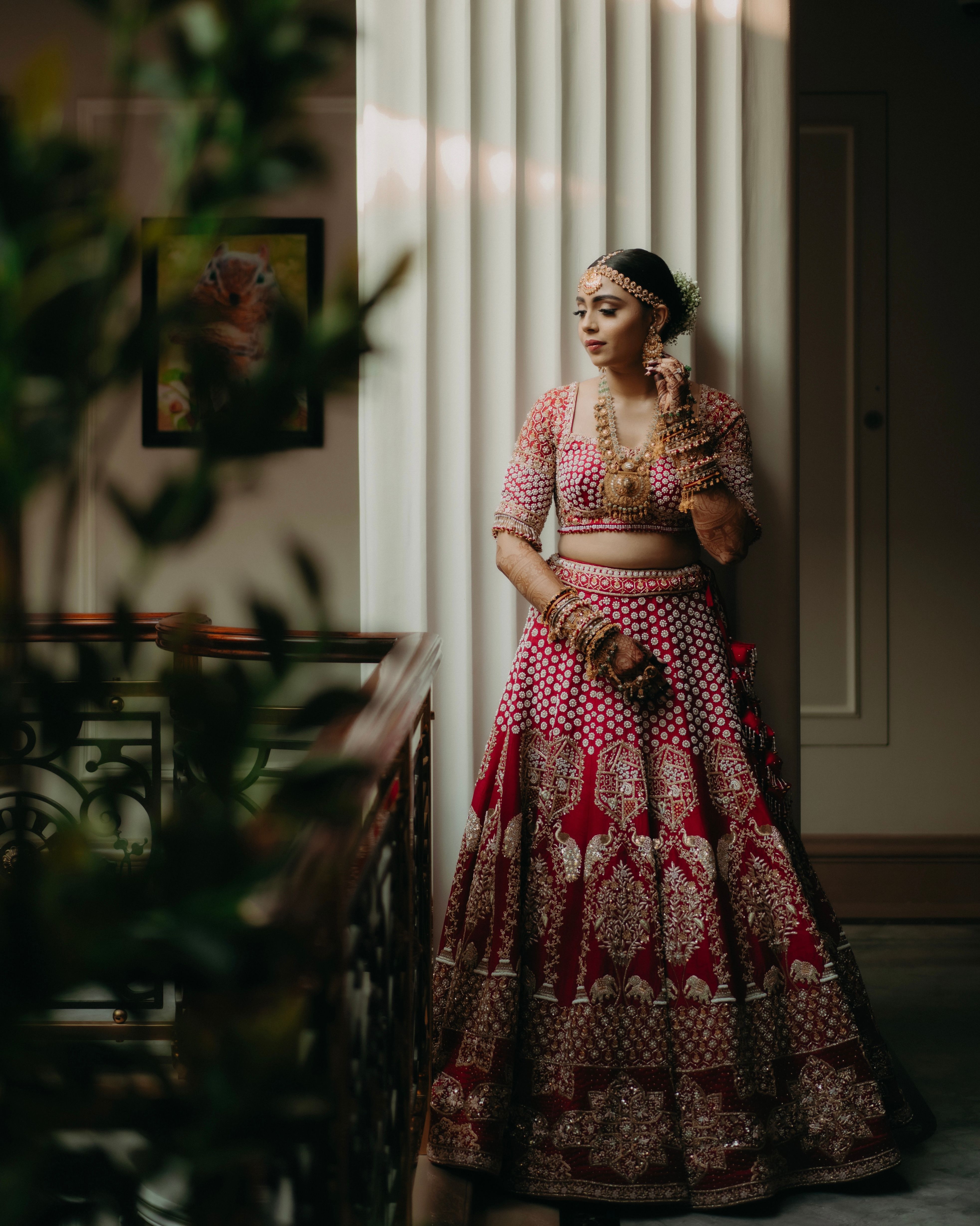 A woman in exquisite traditional bridal attire standing indoors, reflecting elegance and grace.