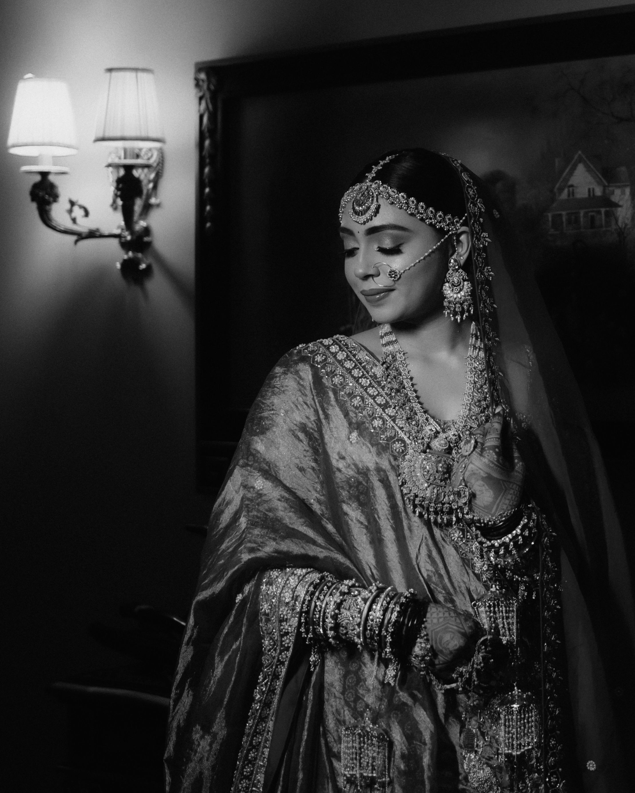 A graceful bride in ornate traditional attire illuminated by soft indoor lighting.