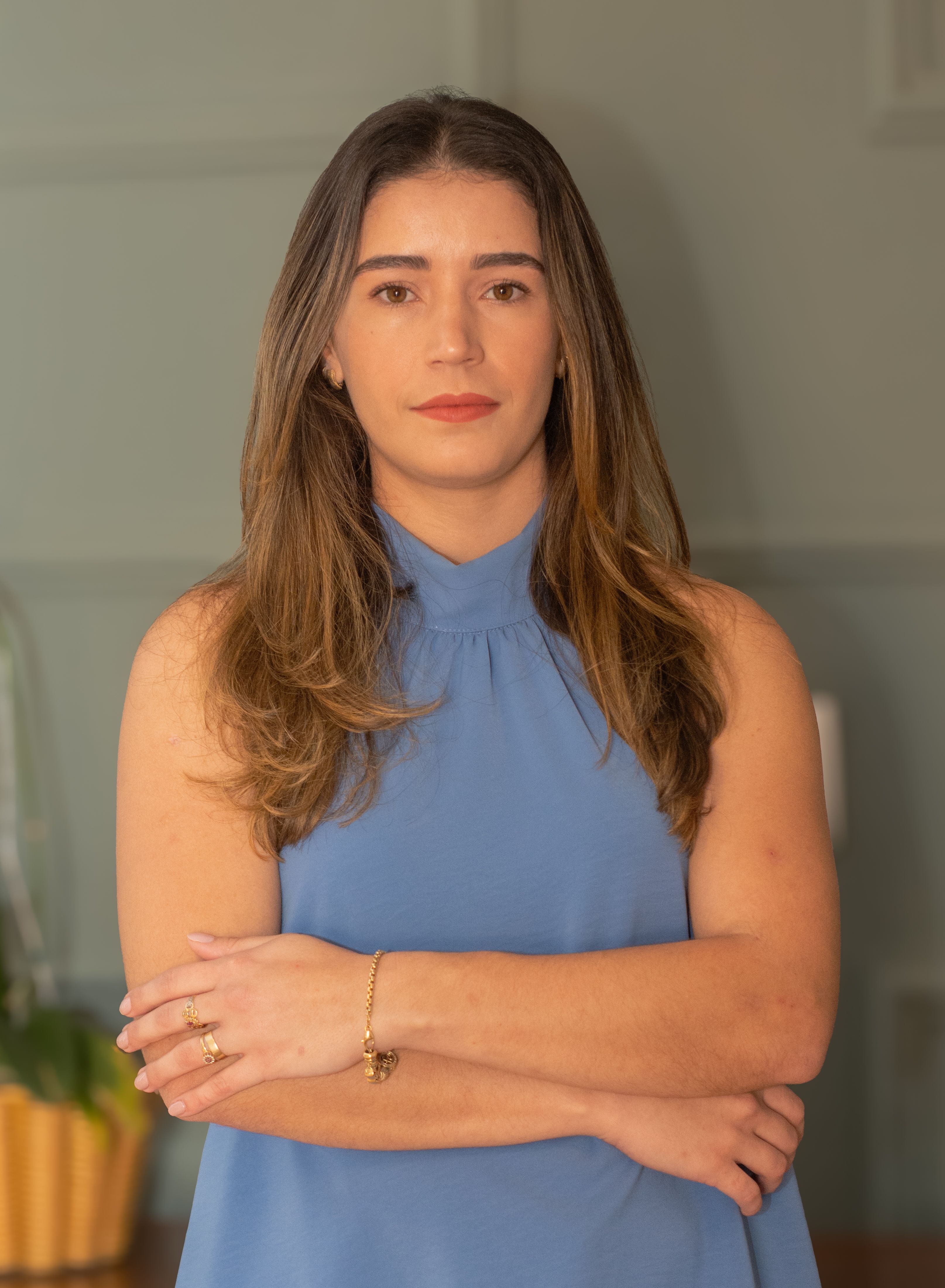 Portrait of a confident woman standing with folded arms indoors, wearing a blue top.