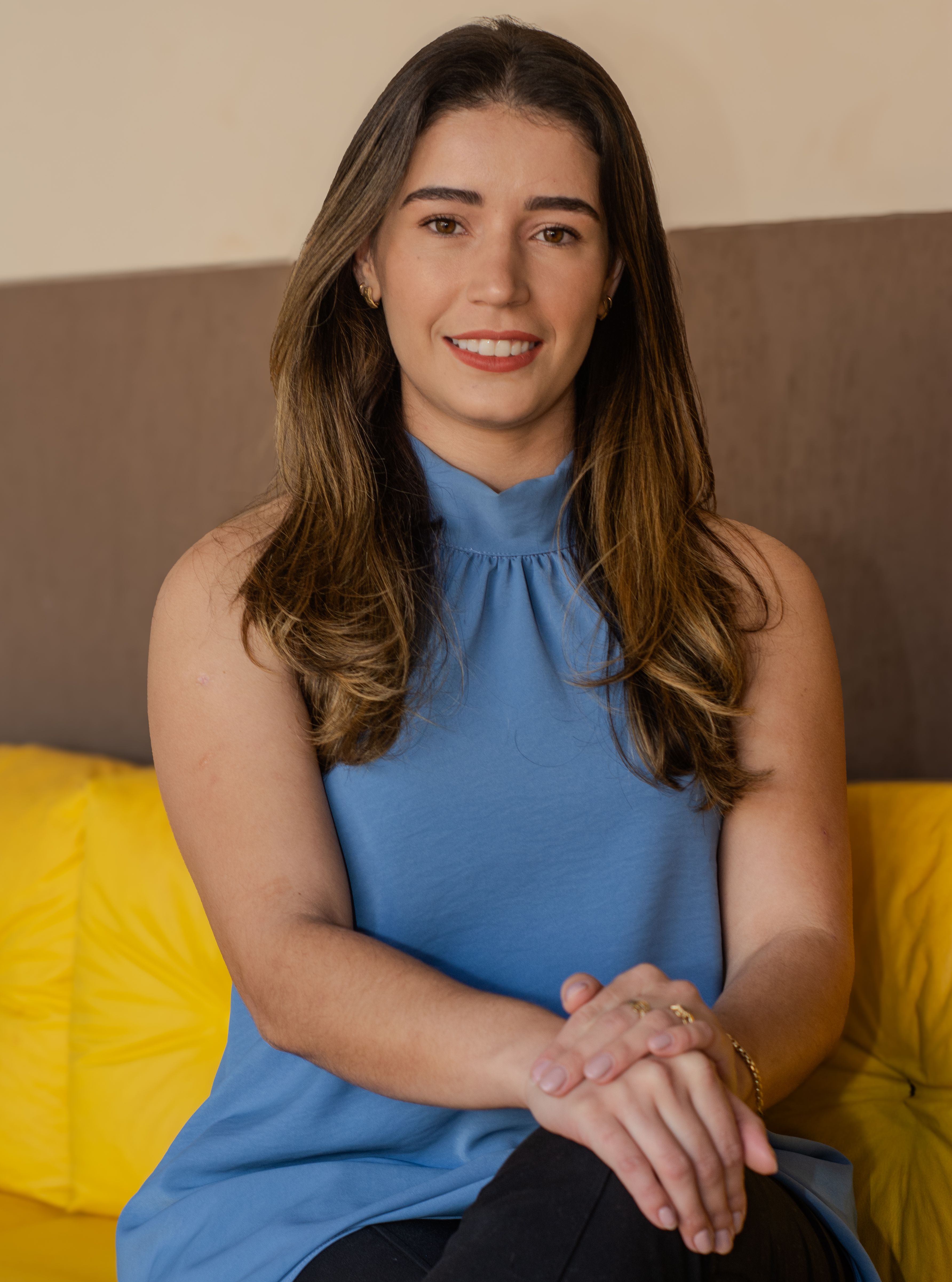 Smiling woman sitting on a yellow couch indoors, wearing a blue top.