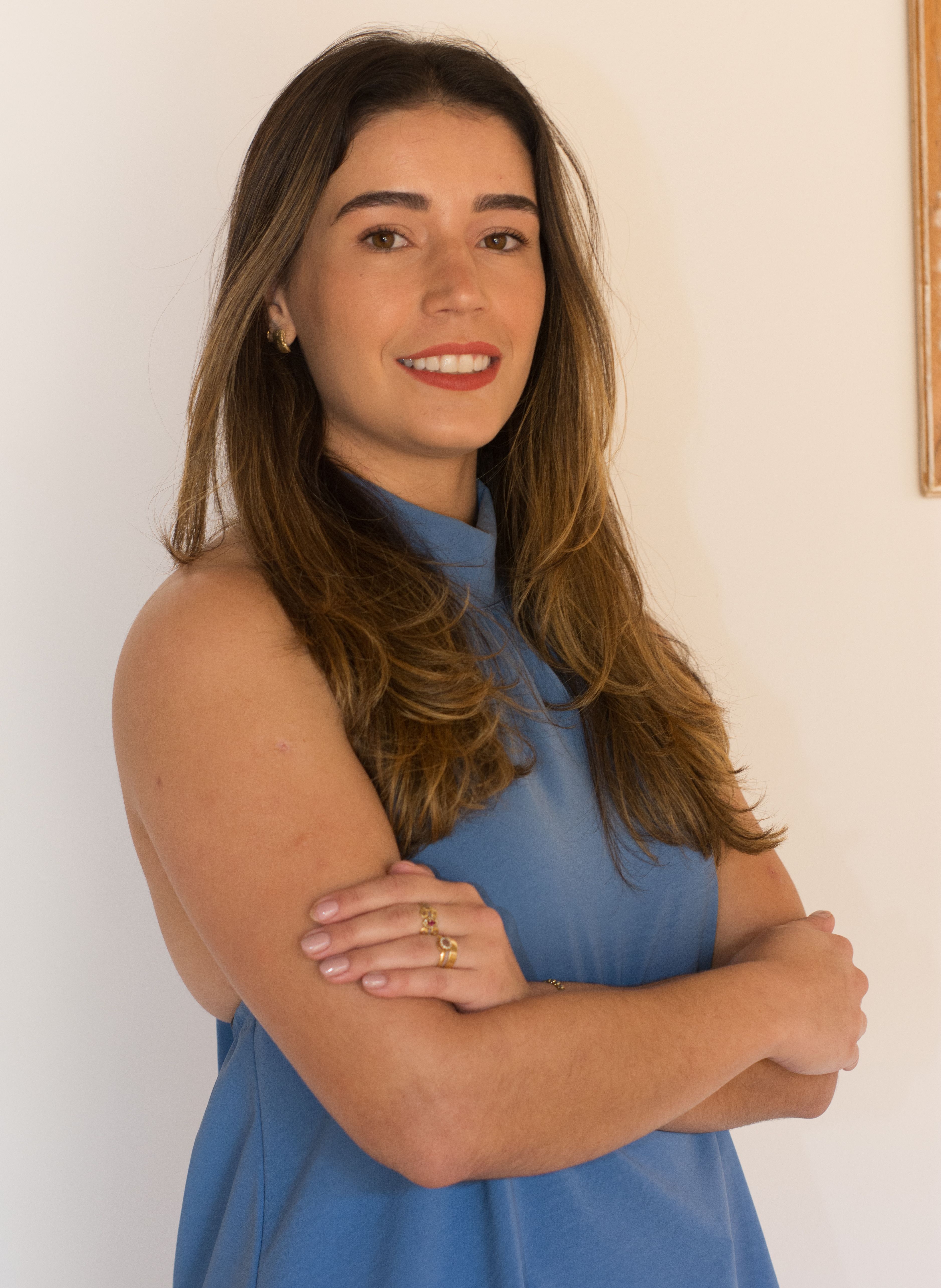Portrait of a confident woman with long hair smiling indoors wearing a blue dress.