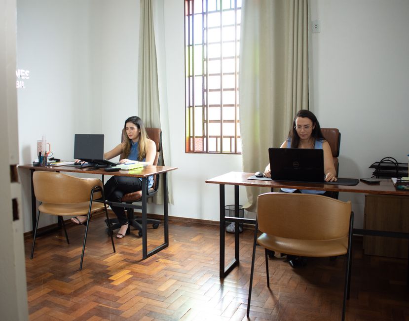 Dos mujeres trabajando en sus computadoras portátiles en una oficina bien iluminada en Tiros, Minas Gerais, Brasil.